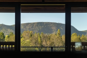 Une vue à travers une fenêtre à cadre en bois, avec une montagne et des arbres au premier plan.