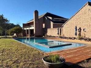 Une piscine avec une terrasse en bois, un bâtiment en briques et des chaises longues.