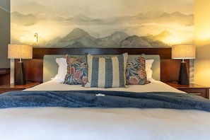 Una cama con cabecera, dos lámparas de noche y un mural con paisaje de montaña en la pared.