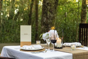 A table set outdoors with a menu, candles, and a glass of red wine. - Plateau Country House (Nature's Valley)