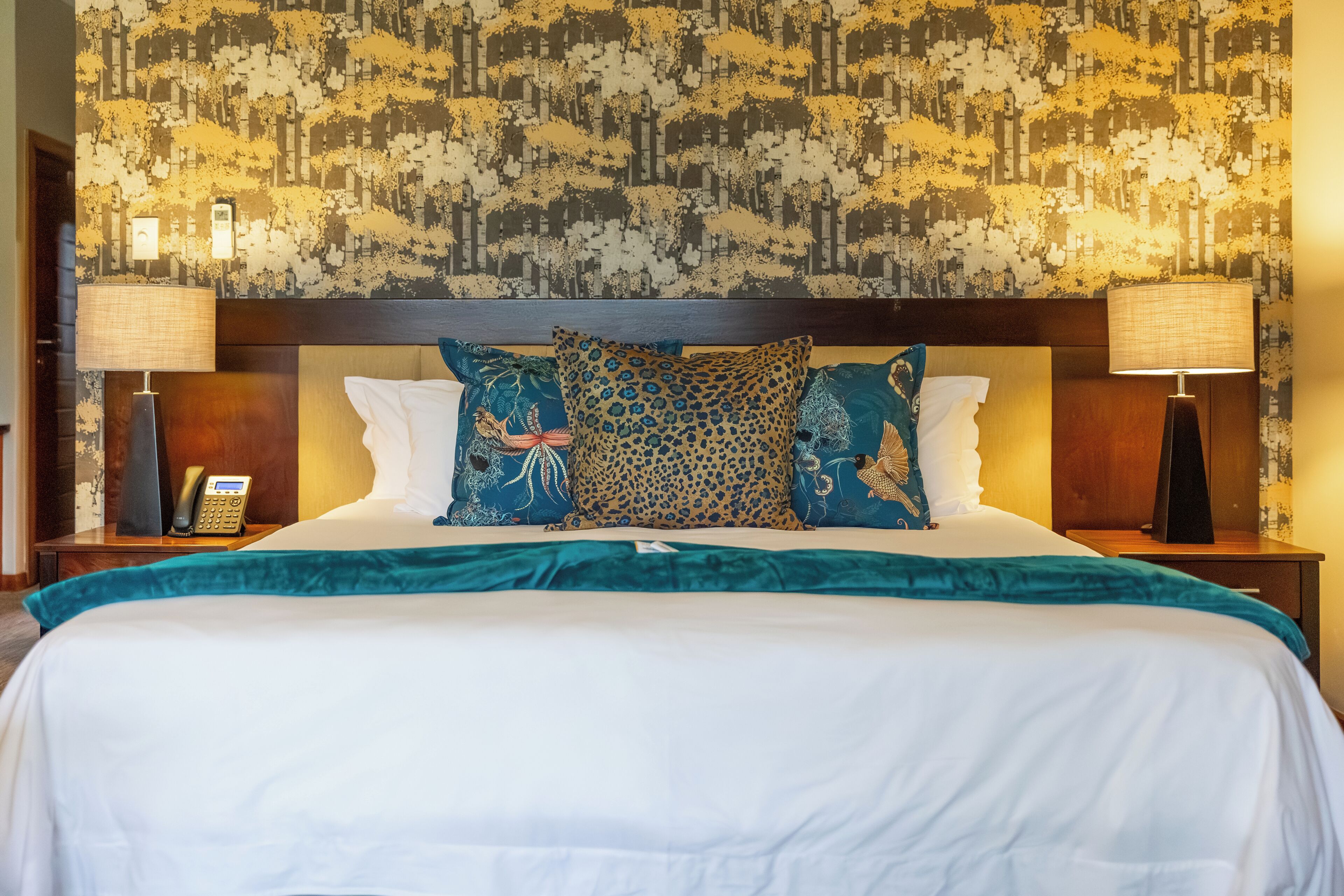 A hotel room with a large bed, two bedside lamps, a telephone, and a patterned wallpaper.