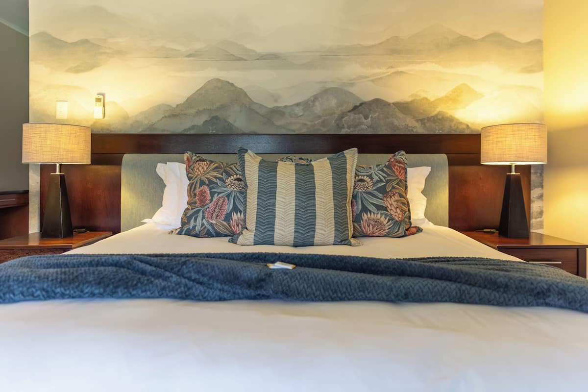 Ein Bett mit blauer Decke, einem Kopfteil mit Blumenmuster und zwei Wandlampen.