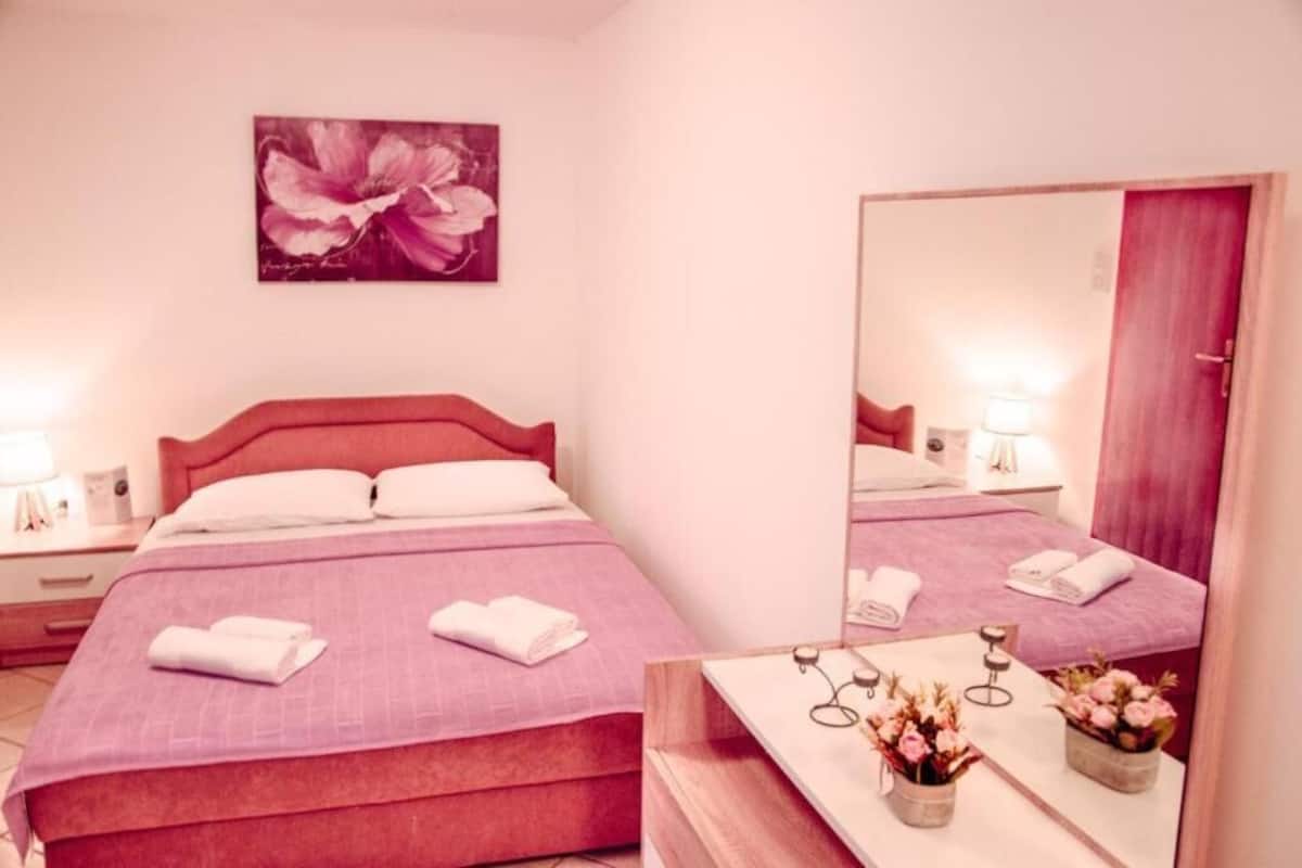 Ein Hotelzimmer mit Bett, Nachttischen, einem Spiegel und einem an der Wand hängenden Blumenbild.