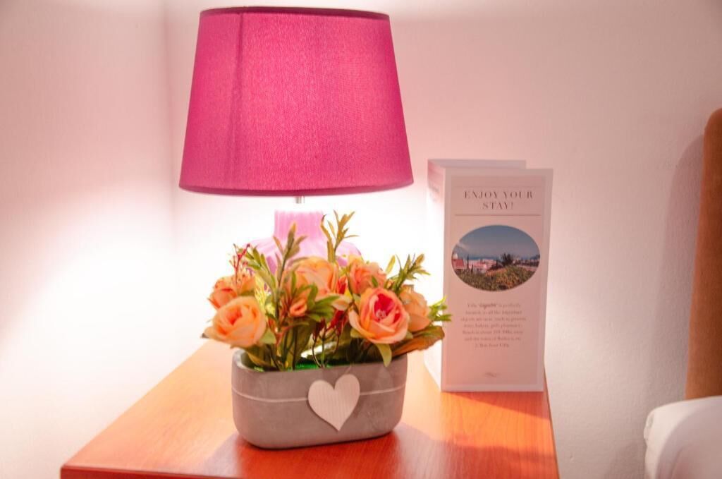 A bedside table with a lamp, a flower arrangement, and a welcome card.