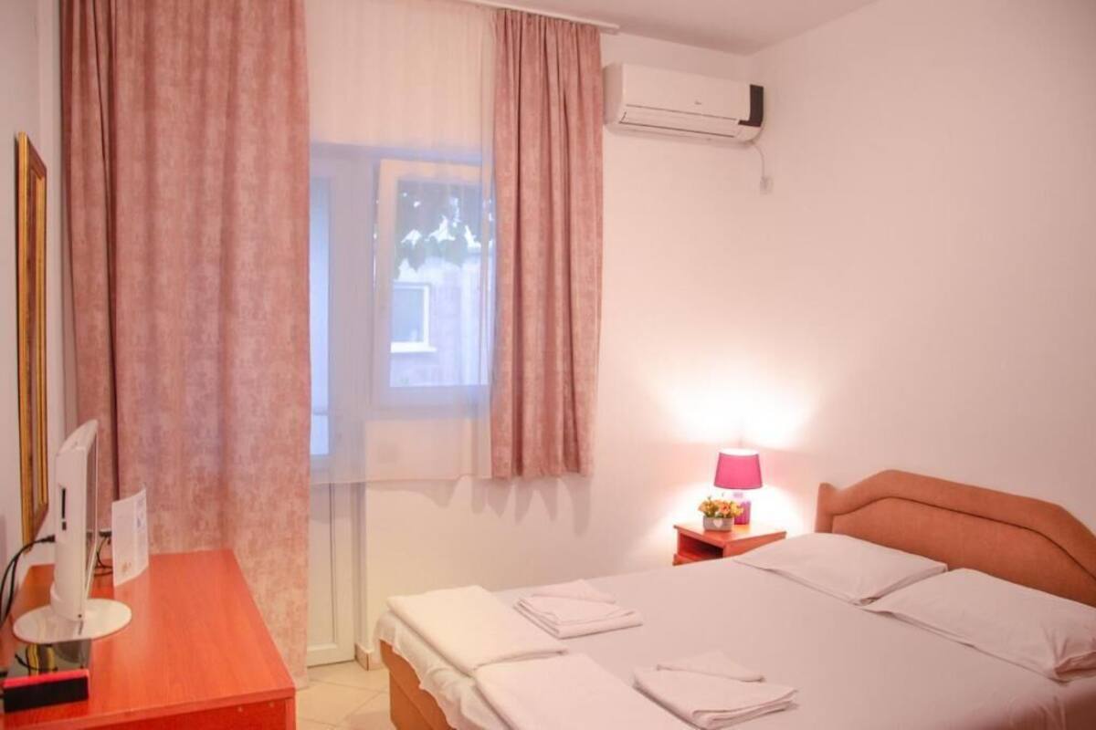 Ein Hotelzimmer mit einem Bett, einem Schreibtisch mit Computer, einer Lampe und einer Klimaanlage.