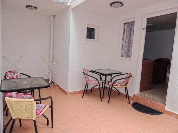 A small patio area with a table and chairs, a door leading to an interior space, and a tiled floor.