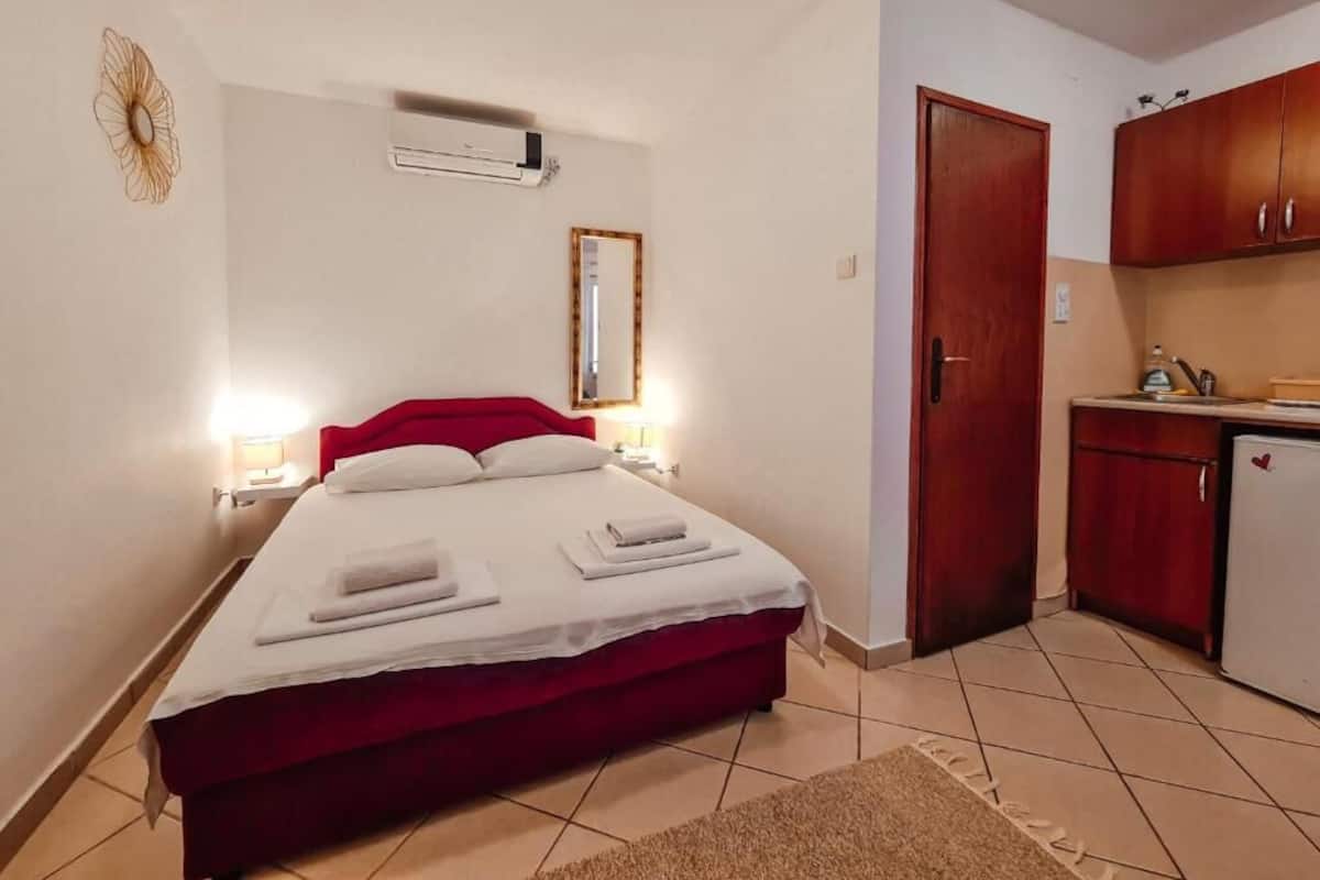 Ein Zimmer mit einem Bett, Nachttischlampen, einem Spiegel, einer Tür und einer Küchenzeile.