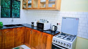 Cozinha com armários de madeira, fogão, micro-ondas e janela com vista para árvores.