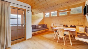 A wooden cabin interior with a sofa, dining table, chairs, and large windows. - Apartment 'Schwalbennest' with Mountain View, Shared Garden and Wi-Fi (Durago di Dentro)
