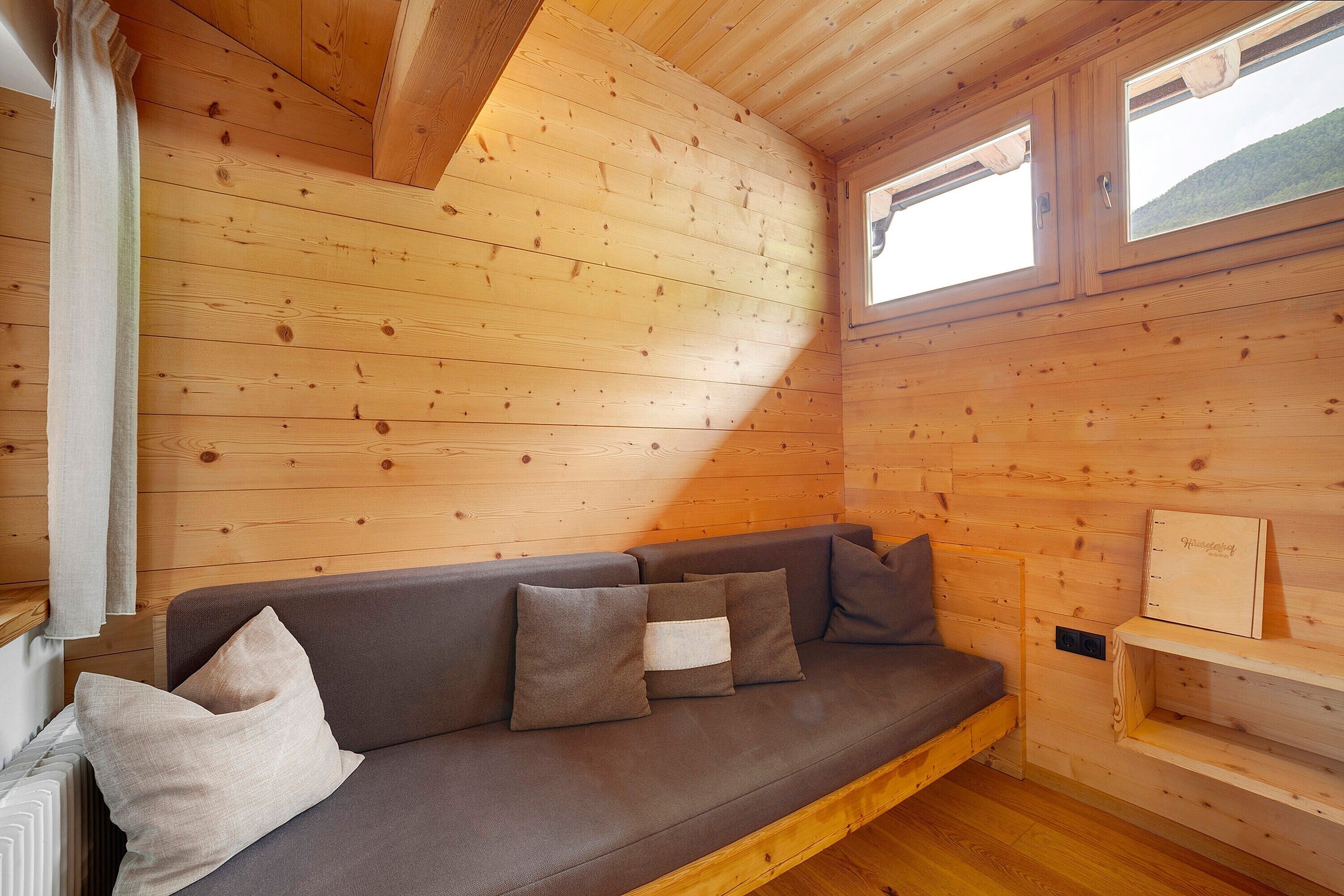 L’intérieur d’un chalet en bois, avec un canapé, des coussins, une fenêtre et une étagère.