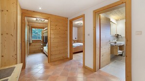 Een houten interieur met een gang die leidt naar een slaapkamer en badkamer, met een bed, een wastafel en een spiegel.