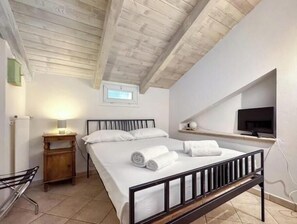 A bedroom with a bed, a bedside table, a lamp, a TV, and a window. - Hostdomus - King Suite (Marina di Andora)