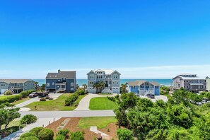 A coastal residential area with houses, a driveway, and a clear view of the ocean. - 2nd Row Designer Cottage w/ Ocean Views, Elevator & Hot Tub (Emerald Isle)