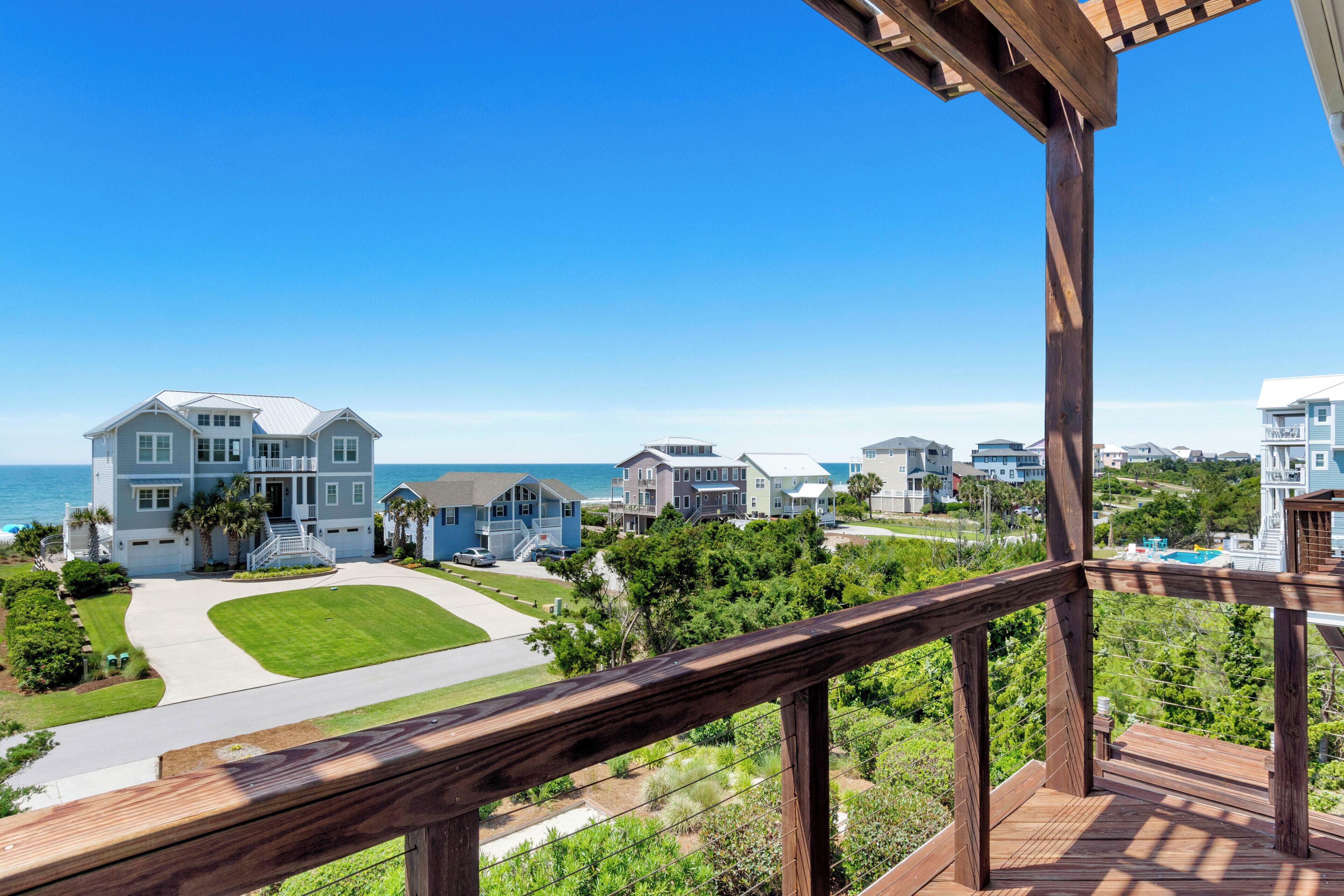 A residential area with multiple houses, a clear blue sky, and a view of the ocean.