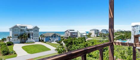 A residential area with multiple houses, a clear blue sky, and a view of the ocean.