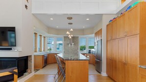 Een moderne keuken met houten kastjes, een centraal eiland, een ingebouwde oven en een groot raam dat voor natuurlijk licht zorgt.