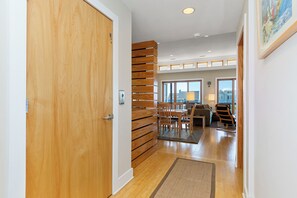 A hallway with a wooden door, a staircase, and a dining area with chairs and a table. - 2nd Row Designer Cottage w/ Ocean Views, Elevator & Hot Tub (Emerald Isle)