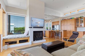 A modern living room with a fireplace, seating area, kitchen, and dining space. - 2nd Row Designer Cottage w/ Ocean Views, Elevator & Hot Tub (Emerald Isle)