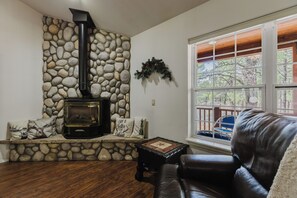 Ein Steinkamin mit Schornstein, ein Ledersofa, ein Holztisch und ein Fenster mit Blick auf Bäume.