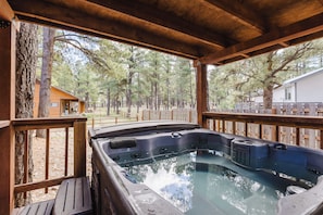 Ein Whirlpool auf einer Holzterrasse mit Blick auf einen Wald und eine Holzhütte.