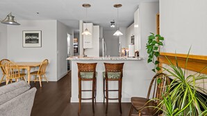 A modern kitchen with a central island, pendant lights, and a dining area with wooden chairs.
