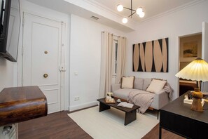 A living room with a sofa, coffee table, lamp, and artwork on the wall. - Discover this sophisticated apartment located on Calle Alonso Cano, in the heart of the Salamanca district, one of Madrid's most exclusive and well-connected areas. (MADRID)