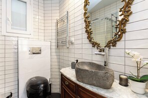 Un baño con lavamanos de piedra, espejo con marco dorado, toallero y una orquídea en maceta.