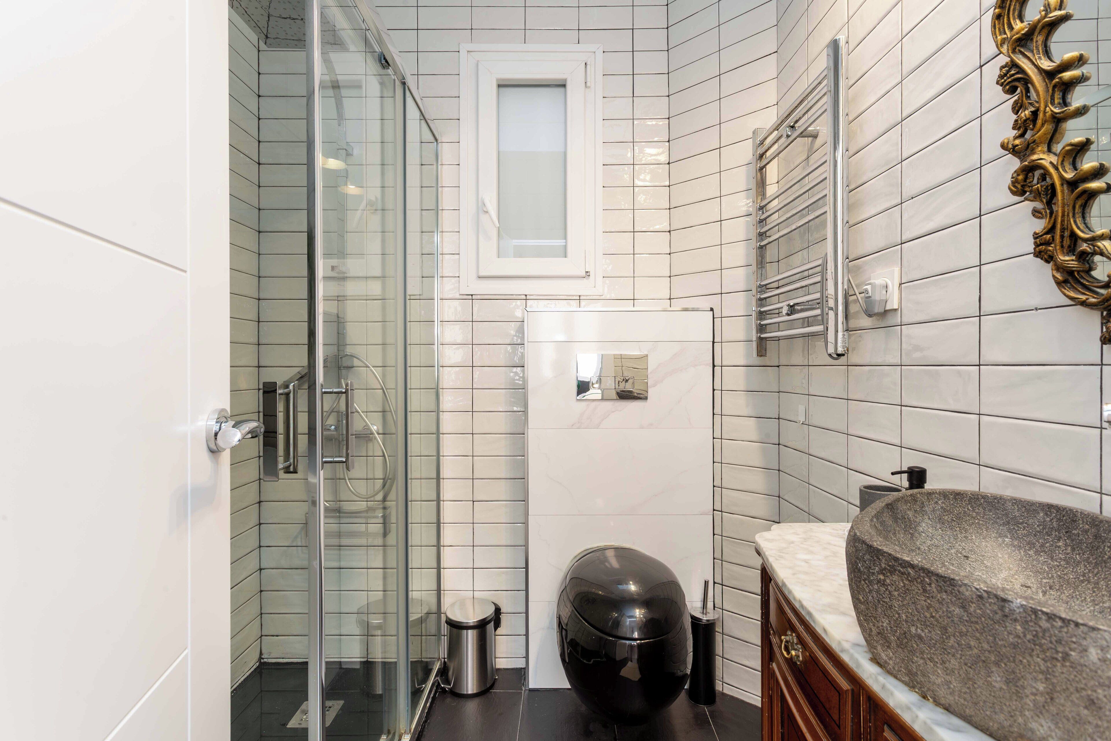 A modern bathroom with a glass shower enclosure, a built-in toilet, and a large stone sink.
