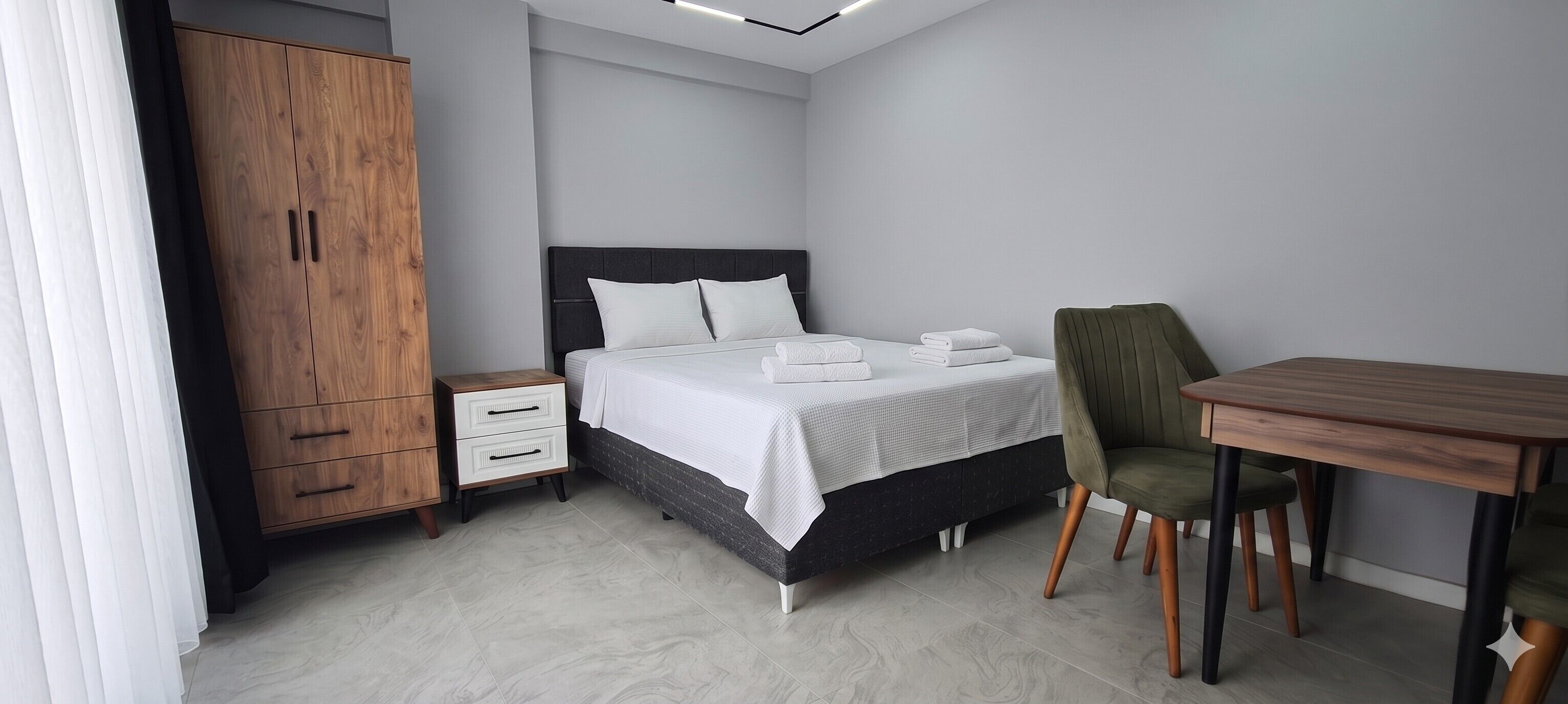 A hotel room with a bed, a desk, a chair, a wardrobe, and a nightstand.