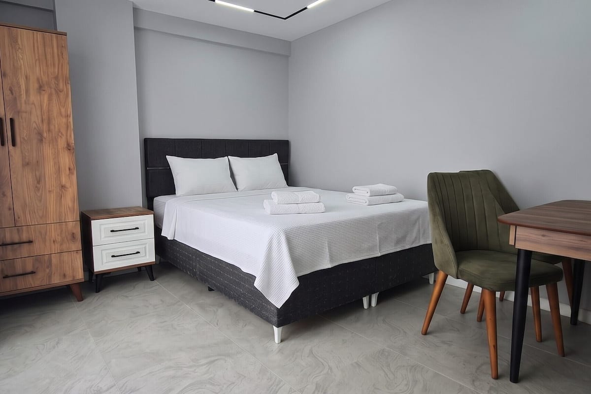 Hotellihuone, jossa on sänky, työpöytä, tuoli, vaatekaappi ja yöpöytä.