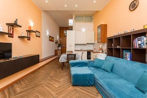Ein Wohnzimmer mit blauem Sofa, Holzboden, einer Küchenzeile und einem Esstisch.