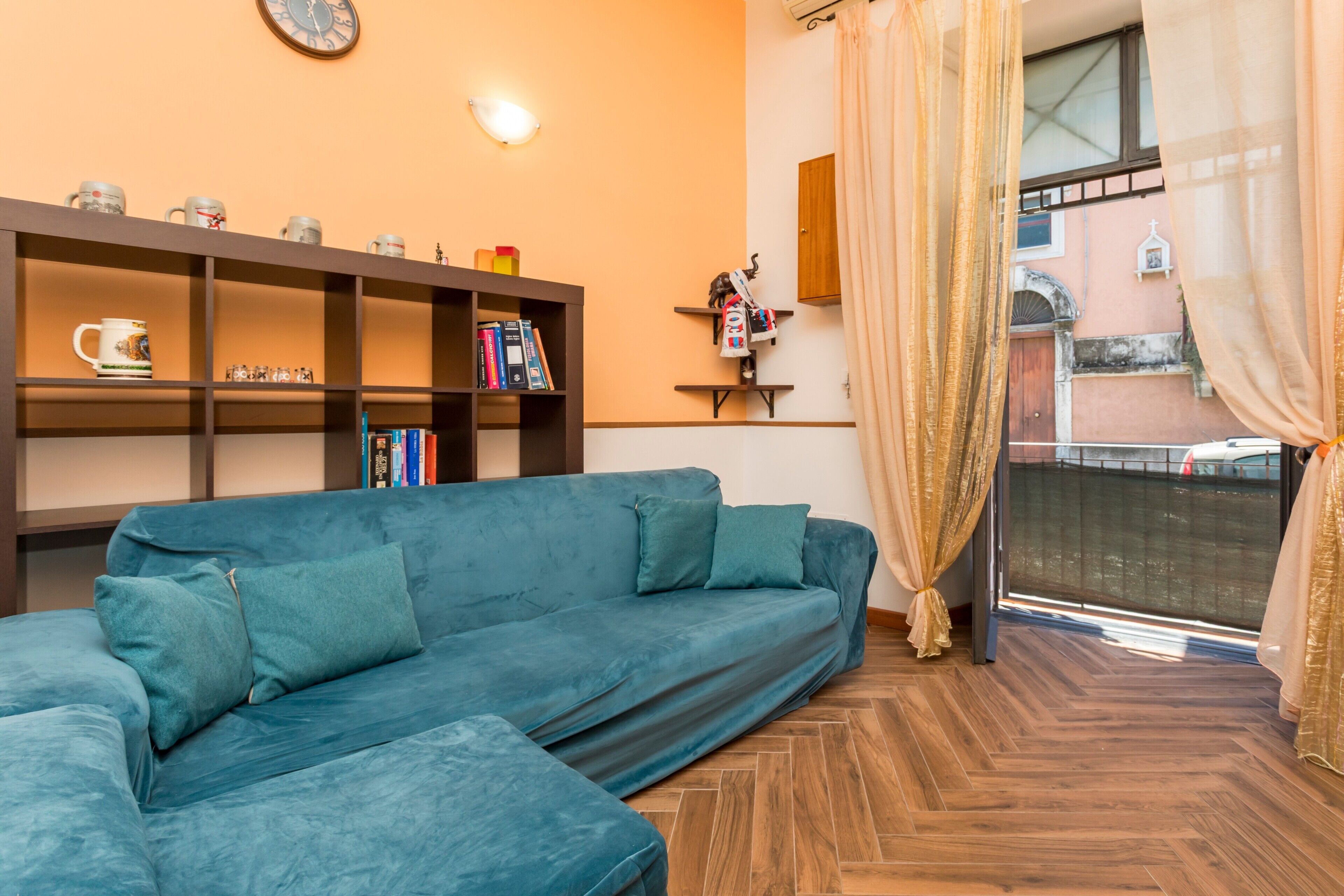 Una sala de estar con un sofá azul, una estantería y una ventana con cortinas.