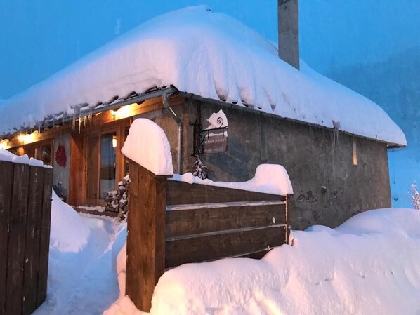 Une cabane en bois avec un toit enneigé et une porte en bois.