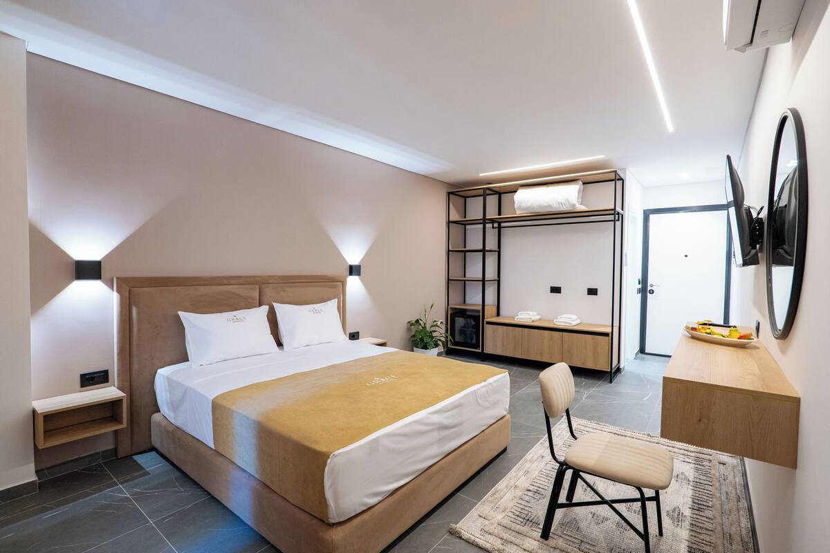 A modern hotel room with a bed, bedside table, desk, chair, and a mirror.