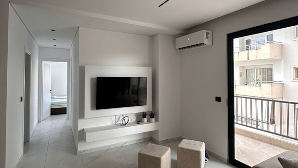 A modern living room with a flat-screen TV, a sofa, and a balcony.