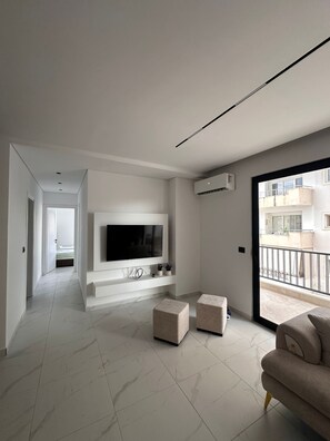 A modern living room with a flat-screen TV, a sofa, and a balcony. - Grace Hotel (Sarande)