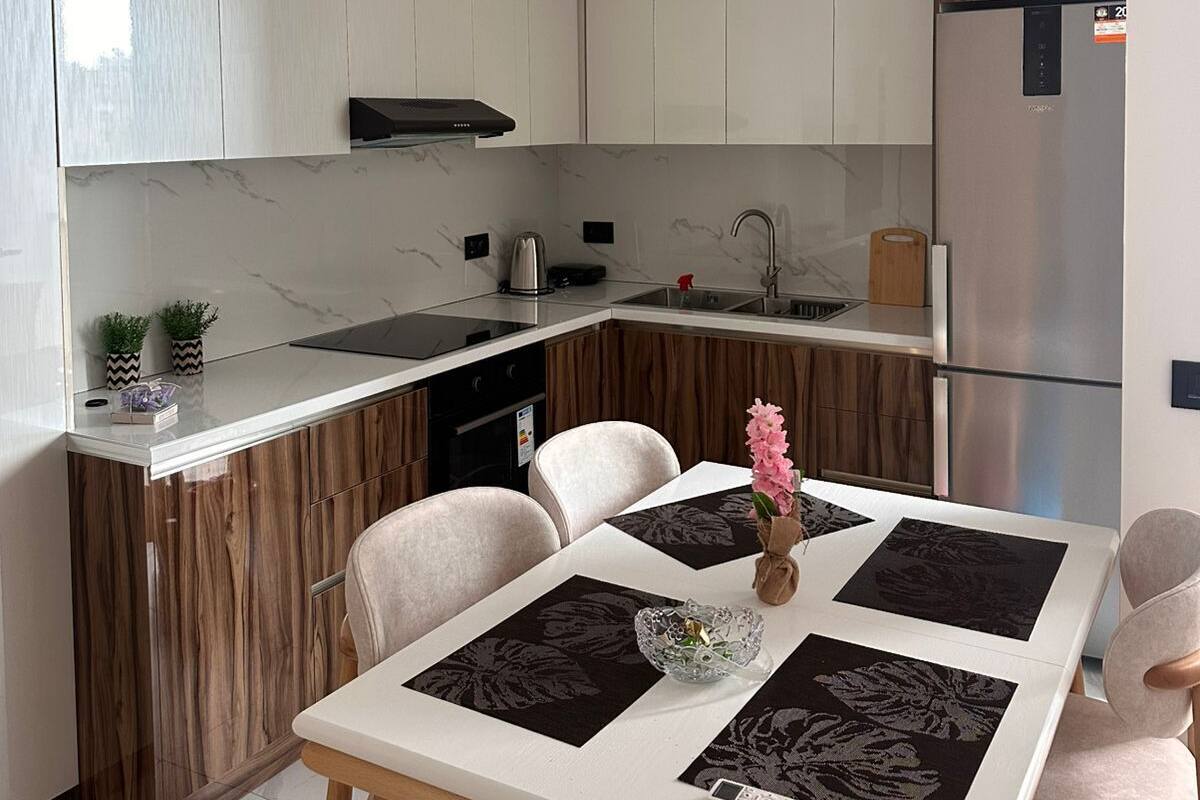 A modern kitchen with a dining area, featuring a built-in oven, stainless steel appliances, and a wooden accent wall.
