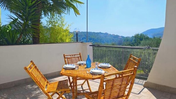 A balcony with a table set for four, surrounded by wicker chairs, overlooking a scenic landscape. - Hostdomus - The house between olive trees and history (Toirano)