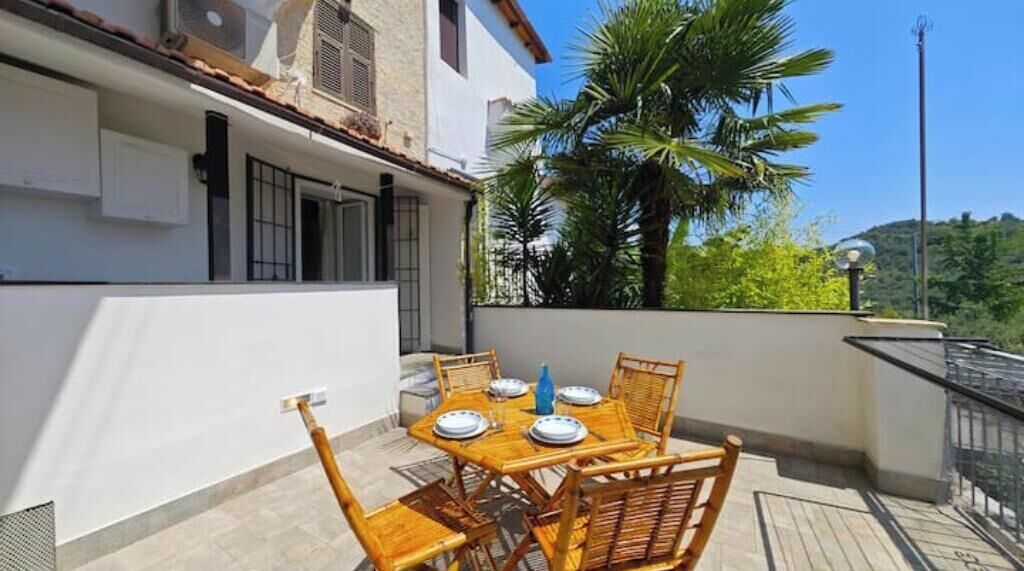 A balcony with a table set for six, surrounded by wicker chairs, and a palm tree in the background.