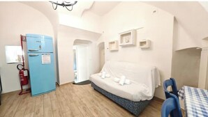 A room with a bed, a blue refrigerator, a table with a checkered tablecloth, and a blue chair. - Hostdomus - The house between olive trees and history (Toirano)