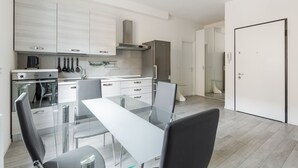 A modern kitchen with a built-in oven, a stainless steel refrigerator, and a glass dining table with chairs. - Mascarella Cozy Studio by Wonderful Italy (Bologna)