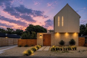 A modern house with a wooden door, a concrete facade, and a well-lit entrance. - Modern Marfa Designer Home w/ Pool & Sleeps 8 (Austin)