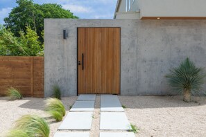 A modern building with a wooden door, a concrete wall, and a gravel pathway leading to the entrance. - Modern Marfa Designer Home w/ Pool & Sleeps 8 (Austin)