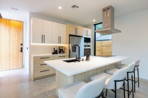 A modern kitchen with a central island, stainless steel appliances, and bar stools. - Modern Marfa Designer Home w/ Pool & Sleeps 8 (Austin)