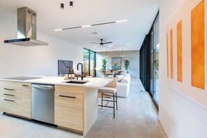 A modern kitchen with a central island, built-in appliances, and a dining area with a sofa and chairs. - Modern Marfa Designer Home w/ Pool & Sleeps 8 (Austin)