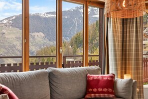 A room with a large window offering a mountain view, a sofa with patterned cushions, and a wicker light fixture. - Pomme de Pin - authentic and spacious (Haute-Nendaz)