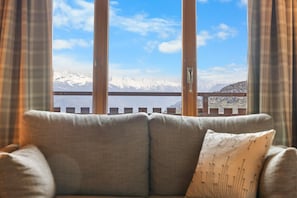 A sofa with a cushion in a room with a view of snow-capped mountains through a window with curtains. - Pomme de Pin - authentic and spacious (Haute-Nendaz)