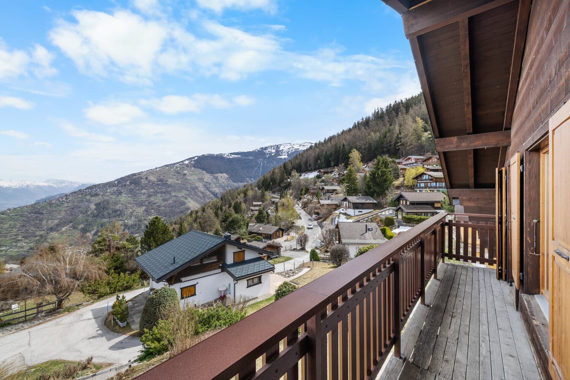 Un balcon en bois donnant sur un village aux maisons traditionnelles, avec une montagne en arrière-plan et un ciel dégagé.