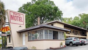 Um motel com placa indicando quarto disponível, um pequeno escritório anexo e área de estacionamento com vários carros.