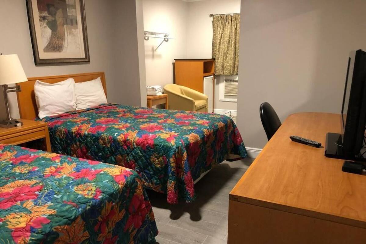 A hotel room with two beds, a desk, a chair, a lamp, a television, and a window with curtains.